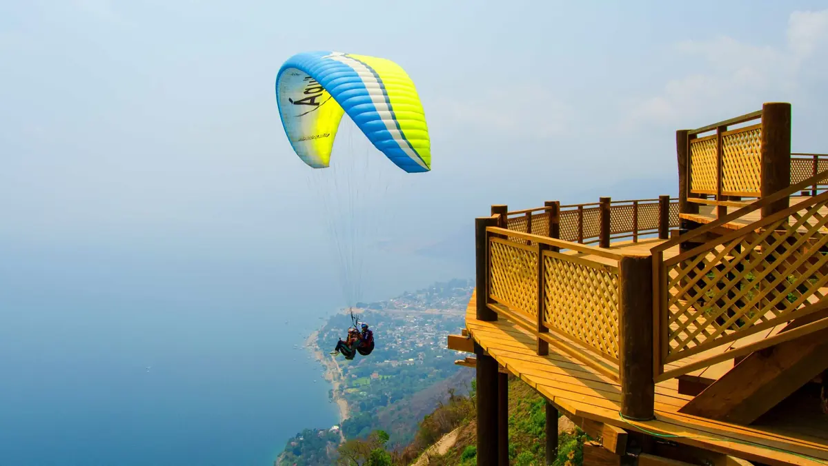 Parapente azul y amarillo volando junto a la plataforma de madera del mirador