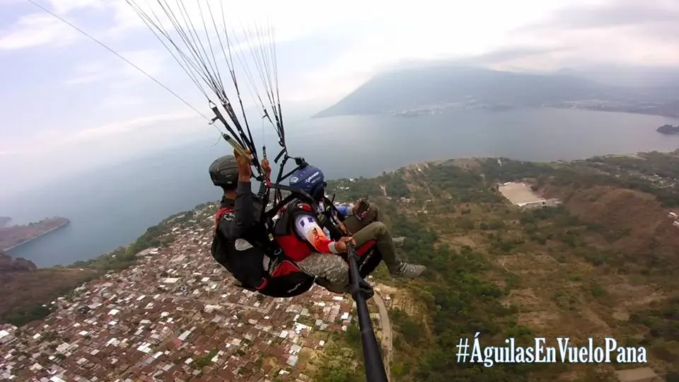 Piloto y pasajero volando en parapente tándem sobre la costa del lago